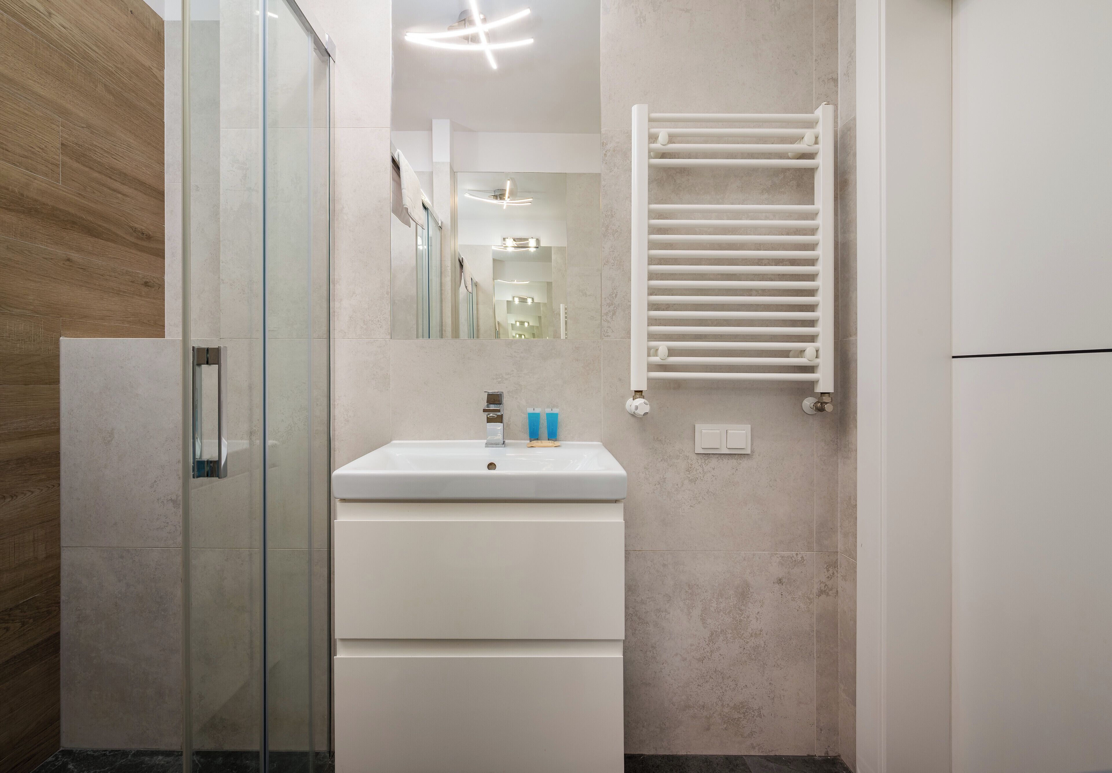 A modern bathroom with a glass shower enclosure, a white sink with a mirror above it, and a towel rack on the wall.