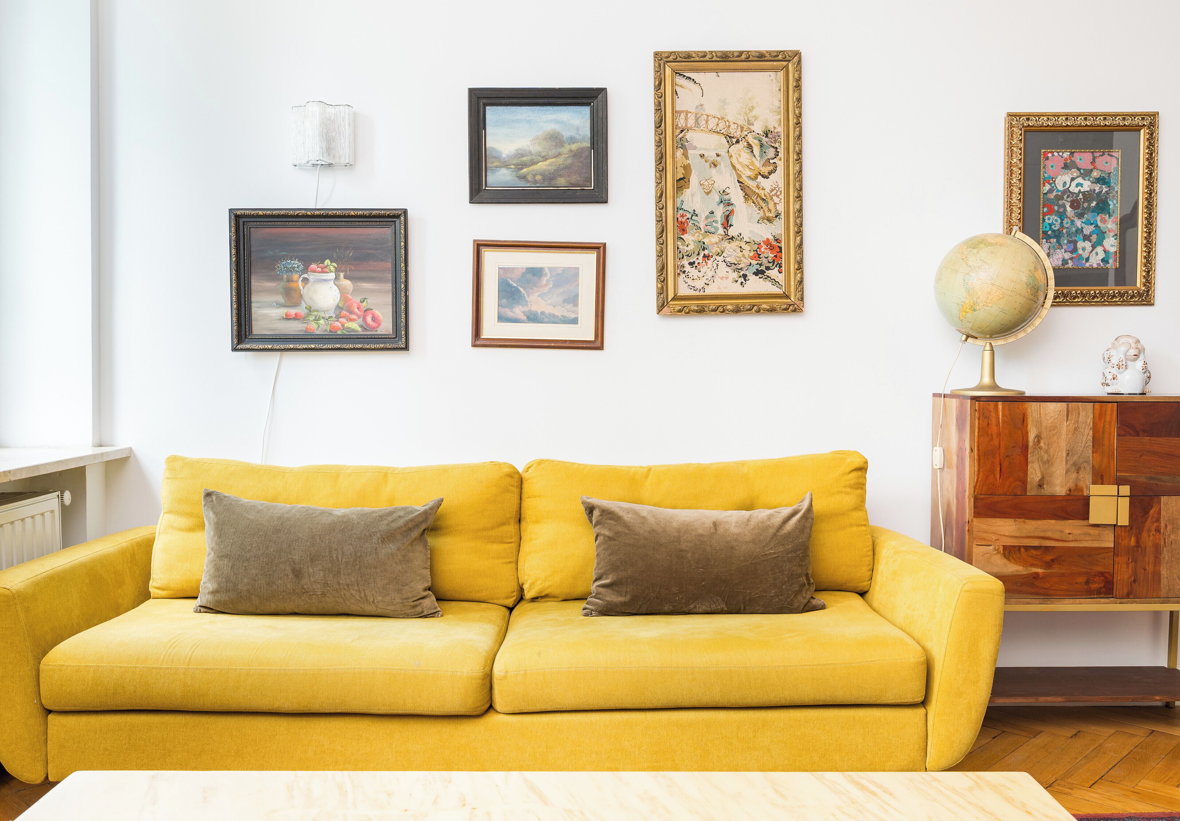 A yellow sofa with cushions, a globe on a wooden cabinet, and framed artwork on the wall.