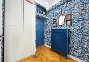 Un couloir avec une porte bleue, une commode bleue et un papier peint à motifs floraux.