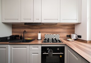 Eine moderne Küche mit weißen Schränken, einer Holz Arbeitsplatte, einem Gasherd, einer Kaffeemaschine und einem Geschirrspüler.