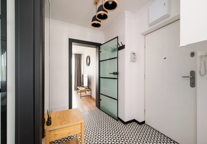 Ein modernes Hotelzimmer mit einem geometrisch gemusterten Boden, einem Holztisch, einer Glastür und einer Deckenleuchte.