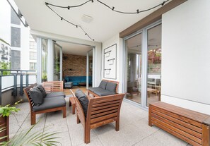 Une terrasse extérieure avec des meubles en bois, un mur en briques et une porte vitrée donnant sur un espace intérieur.