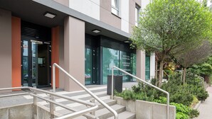 Ein Gebäudeeingang mit Treppe, Metallgeländern und einem kleinen Gartenbereich mit Pflanzen.