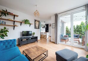 Un salon moderne comprenant un canapé, une table basse, un téléviseur et un balcon aménagé avec du mobilier d’extérieur.