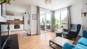 Ein modernes Wohnzimmer mit Holzboden, einem grauen Sessel, einem blauen Sofa, einem Couchtisch und einer Küche im Hintergrund.