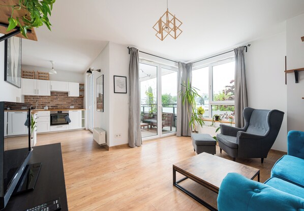 Un salon moderne avec un plancher en bois, un fauteuil gris, un canapé bleu, une table basse et une cuisine en arrière-plan.