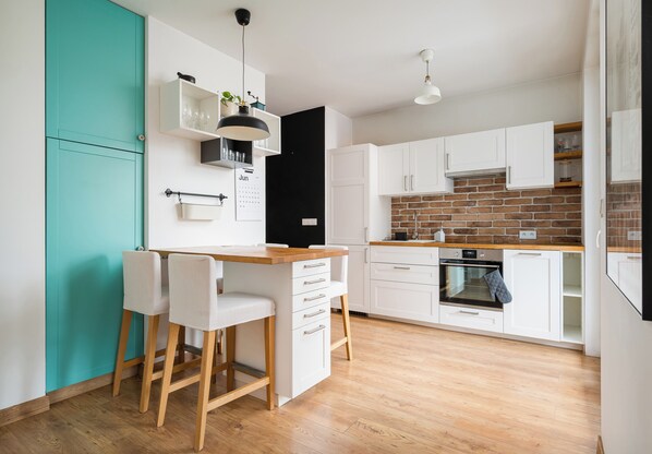 Een moderne keuken met witte kastjes, een achterwand van baksteen en een houten aanrecht.