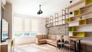 Una sala de estar moderna con un sofá modular, una mesa de comedor con sillas y estanterías empotradas con un fondo de pared de ladrillo.