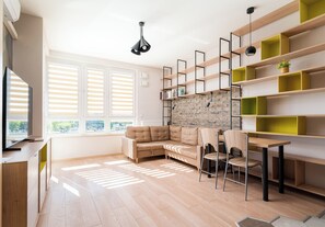 Een moderne woonkamer met een hoekbank, een eettafel met stoelen en ingebouwde planken tegen een achtergrond van een bakstenen muur.