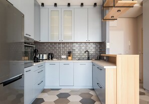 Eine moderne Küche mit hellblauen Schränken, einem Edelstahl-Kühlschrank, einer sechseckig gemusterten Spritzschutzwand und einer Holz Arbeitsplatte.