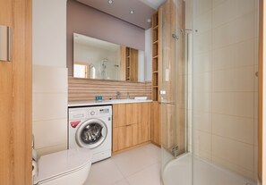 Een moderne badkamer met een wasmachine, toilet en douchecabine van glas.