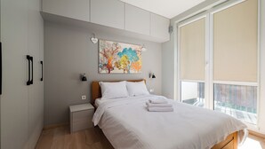 Un dormitorio con una cama, mesitas de noche, un cuadro y una ventana.