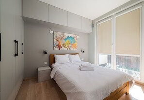 Ein Schlafzimmer mit einem Bett, Nachttischen, einem Gemälde und einem Fenster.