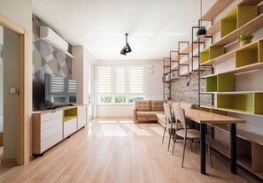 Eine moderne Küche mit Einbauofen, ein Essbereich mit Holztisch und Stühlen sowie ein Fernseher links.