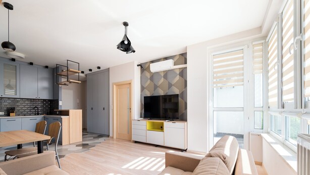 Una sala de estar moderna con un sofá, una mesa de comedor y una zona de cocina con armarios y un televisor.