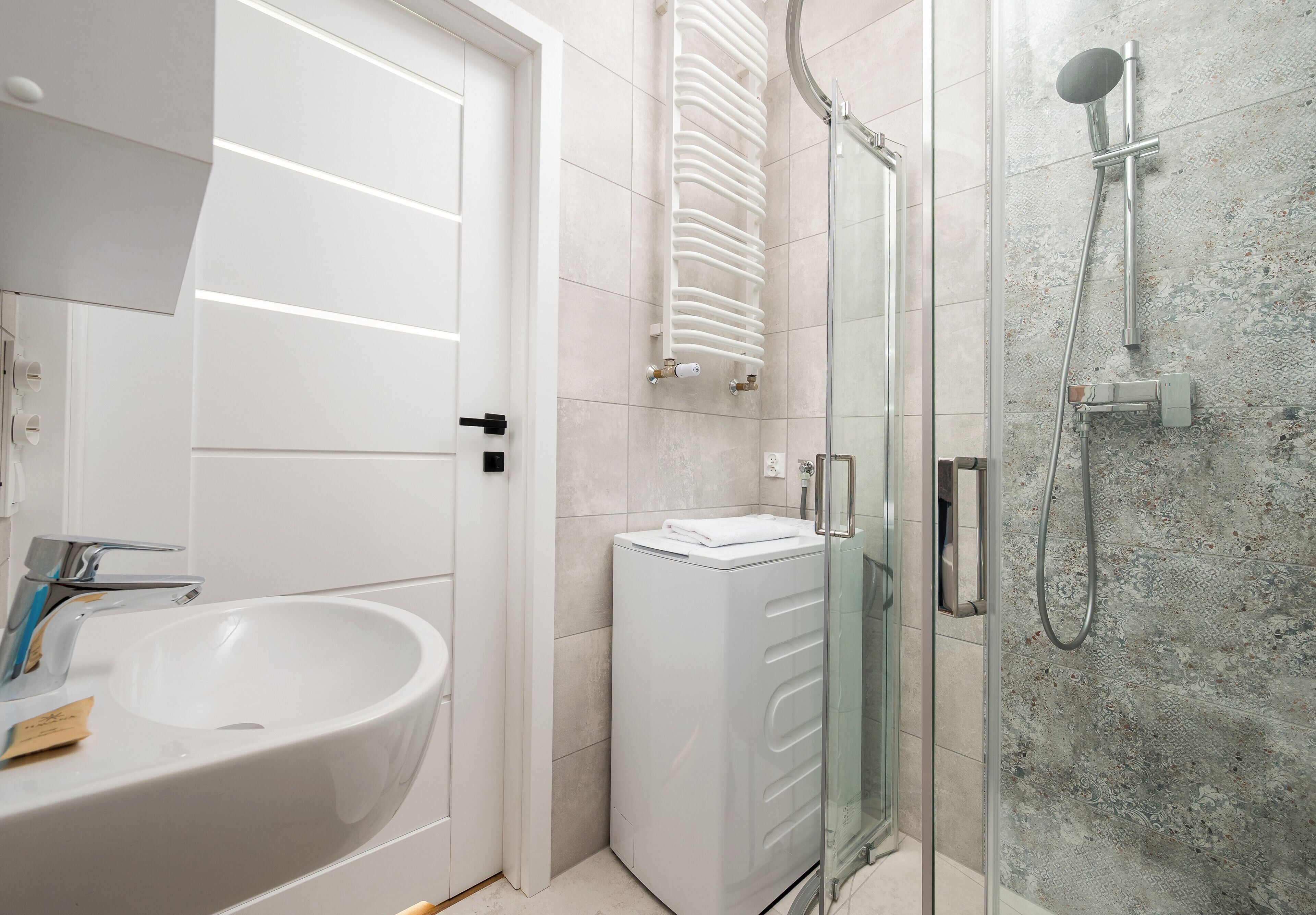 A bathroom with a white sink, a glass shower enclosure, and a white radiator.