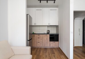 Eine kompakte Küche mit weißen Schränken, einem Edelstahlkühlschrank und einem schwarzen Geschirrspüler.