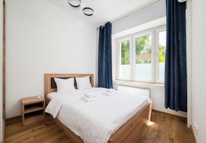 Ein Schlafzimmer mit einem hölzernen Bett, weißer Bettwäsche, einem Nachttisch und einem Fenster mit Vorhängen.