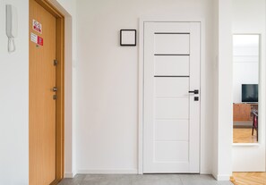 Ein Hotelzimmer mit einer Holztür, einer weißen Tür mit horizontalen Linien, einem kleinen gerahmten Bild, einem Telefon und einem Fernseher.