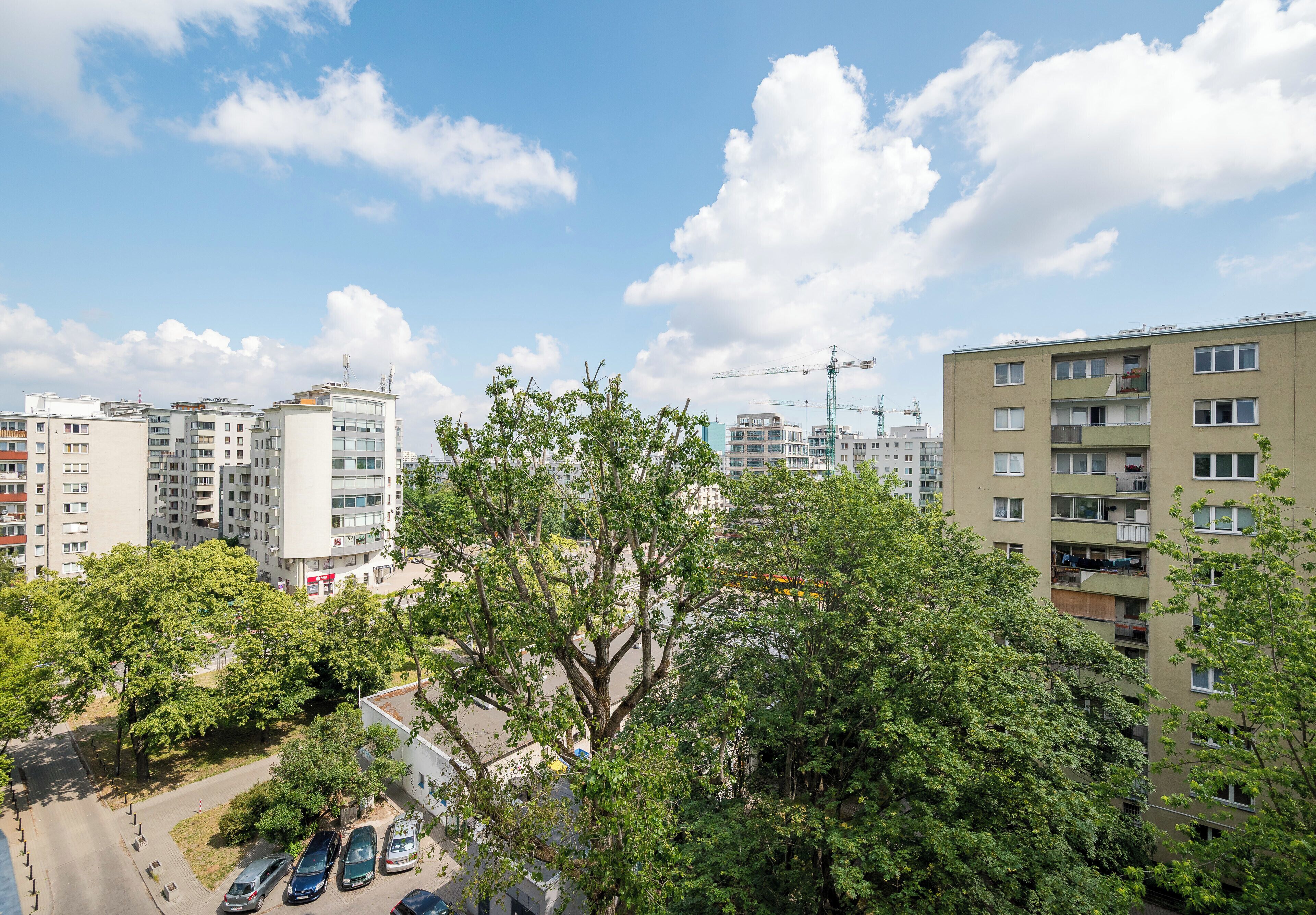 Un immeuble résidentiel à plusieurs étages, doté de balcons, d’un espace de stationnement et de grues de construction en arrière-plan.