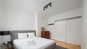 Et soveværelse med seng, et natbord, et kommode, en garderobe og et mønstret tæppe.