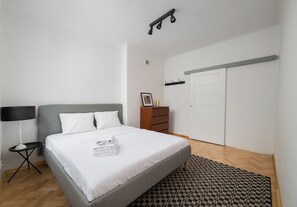 A bedroom with a bed, a nightstand, a dresser, a wardrobe, and a patterned rug. - Metro Racławicka Exclusive Apartment (Warszawa)