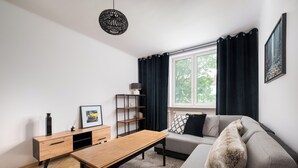 En moderne stue med sofa, sofabord i træ, skænk og et stort vindue med gardiner.