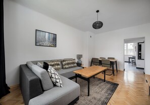 A modern living room with a grey sofa, a wooden coffee table, and a cityscape painting on the wall. - Metro Racławicka Exclusive Apartment (Warszawa)