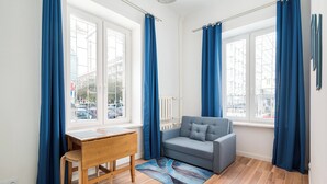 A room with a wooden floor, a grey sofa, a wooden table with a chair, and blue curtains on the windows. - Warecka City Center Living Apartment (Warszawa)