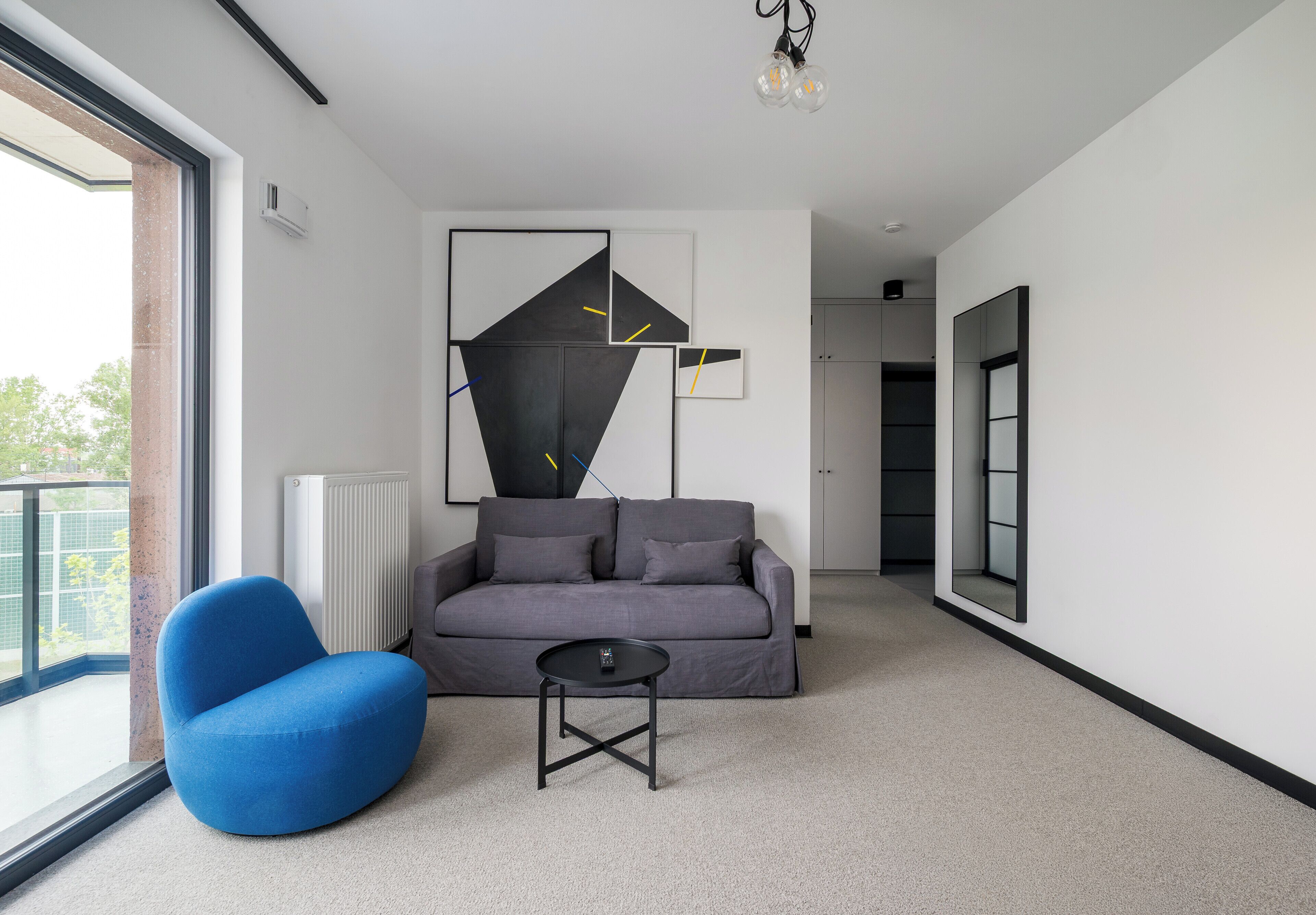 Una sala de estar moderna con un sofá gris, un sillón azul, una mesita pequeña y arte abstracto en la pared.