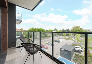 Ein Balkon mit einem Stuhl, Blick auf einen Parkplatz und ein Gebäude gegenüber.