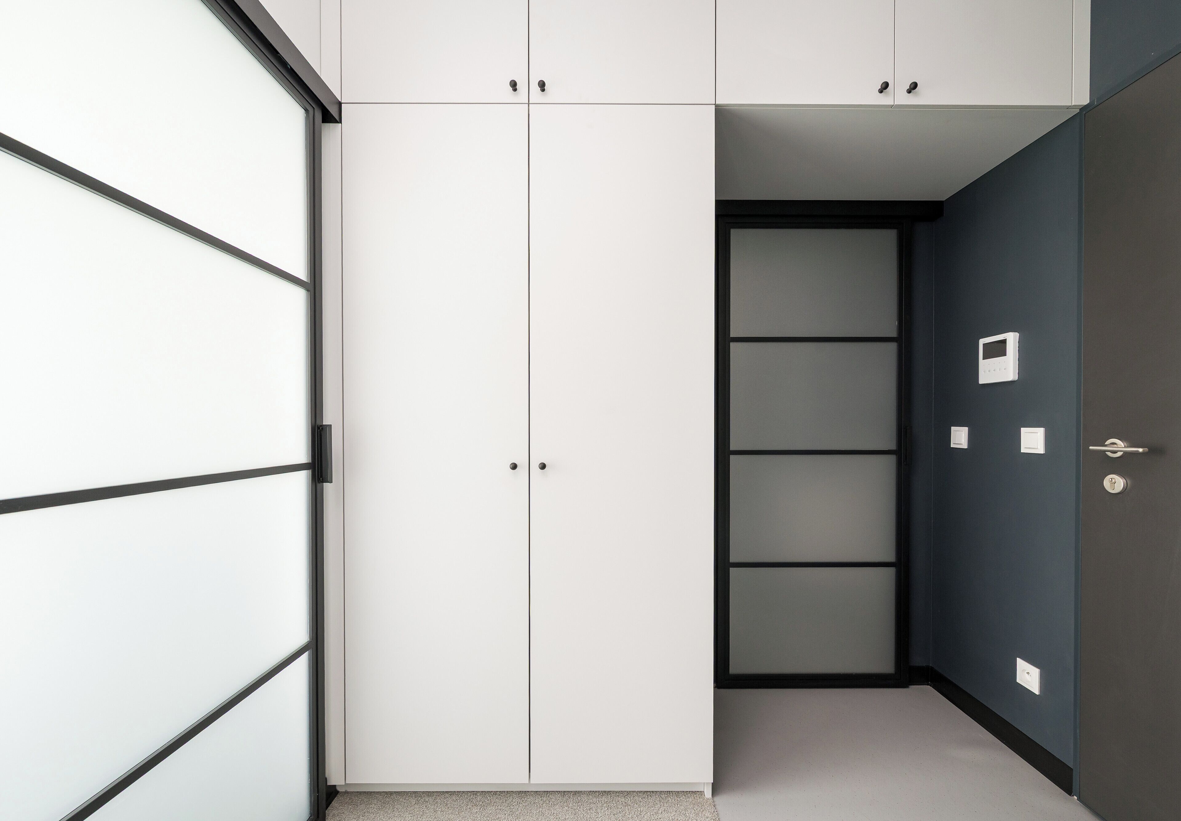 A modern room with a wardrobe, a door, and a wall-mounted thermostat.
