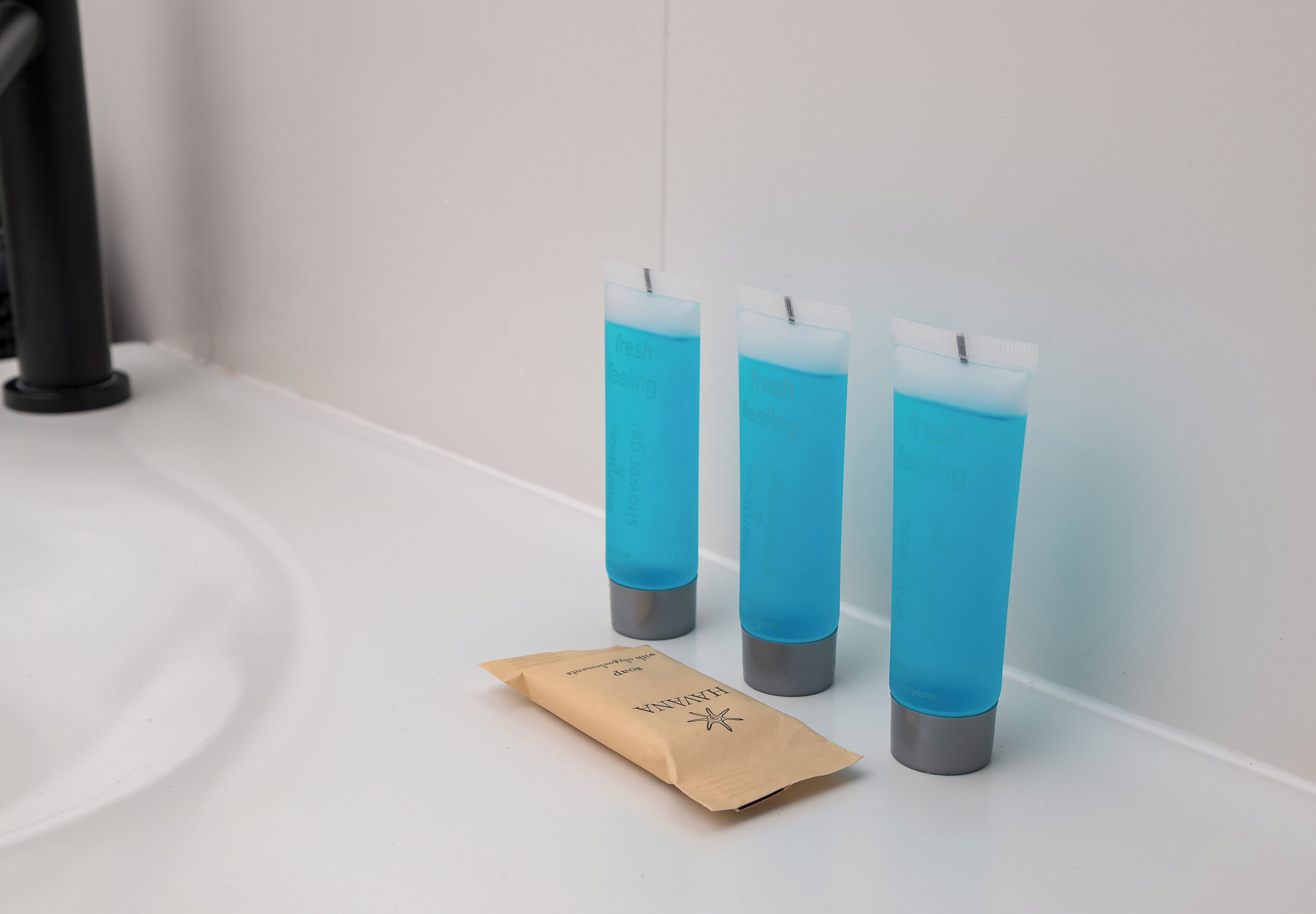 Tres botellas azules con etiquetas, una bolsa de papel marrón y una tubería negra sobre una superficie blanca.