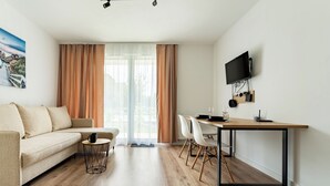 Ein modernes Wohnzimmer mit einer Couch, einem Esstisch mit Stühlen, einem an der Wand befestigten Fernseher und einem großen Fenster mit Vorhängen.