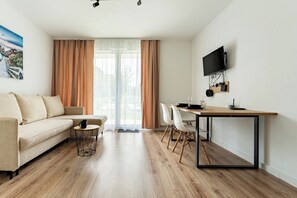 Ein modernes Wohnzimmer mit einer Couch, einem Esstisch mit Stühlen, einem an der Wand befestigten Fernseher und einem großen Fenster mit Vorhängen.