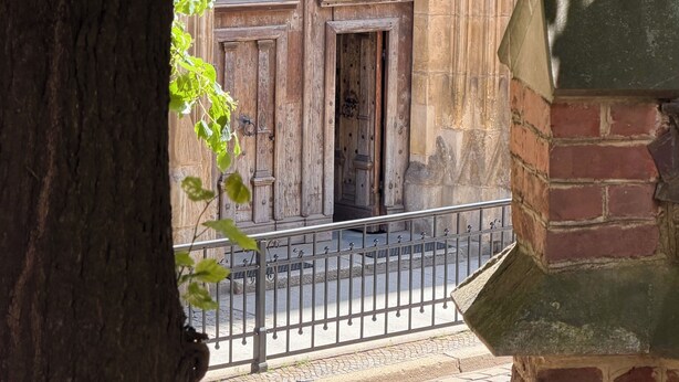 Une vue d’un bâtiment avec deux grandes portes en bois, une rambarde en métal et un mur en pierre.