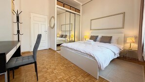 Une chambre à coucher comprenant un lit, des tables de chevet, un bureau, une chaise, un lustre et un miroir.