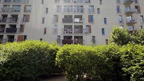 Un immeuble résidentiel à plusieurs étages, doté de balcons, d’une enseigne et d’un beau parterre bien entretenu au premier plan.