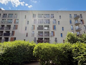 Ein mehrstöckiges Wohngebäude mit Balkonen, einer Schautafel und einem gepflegten Heckenstreifen im Vordergrund.
