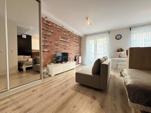 Ein modernes Wohnzimmer mit Backsteinwand, einem Flachbildfernseher, einer Couch und einer Essecke mit einem weißen Schrank.