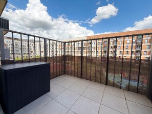 Ein Balkon mit einem Maschendrahtzaun, Fliesenboden und Blick auf mehrstöckige Wohngebäude.