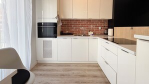 Une cuisine moderne avec des meubles blancs, un four noir et un mur de fond en briques.