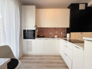 A modern kitchen with white cabinets, a black oven, and a brick backsplash. - Zakładowa Modern Living Studio (Wrocław)