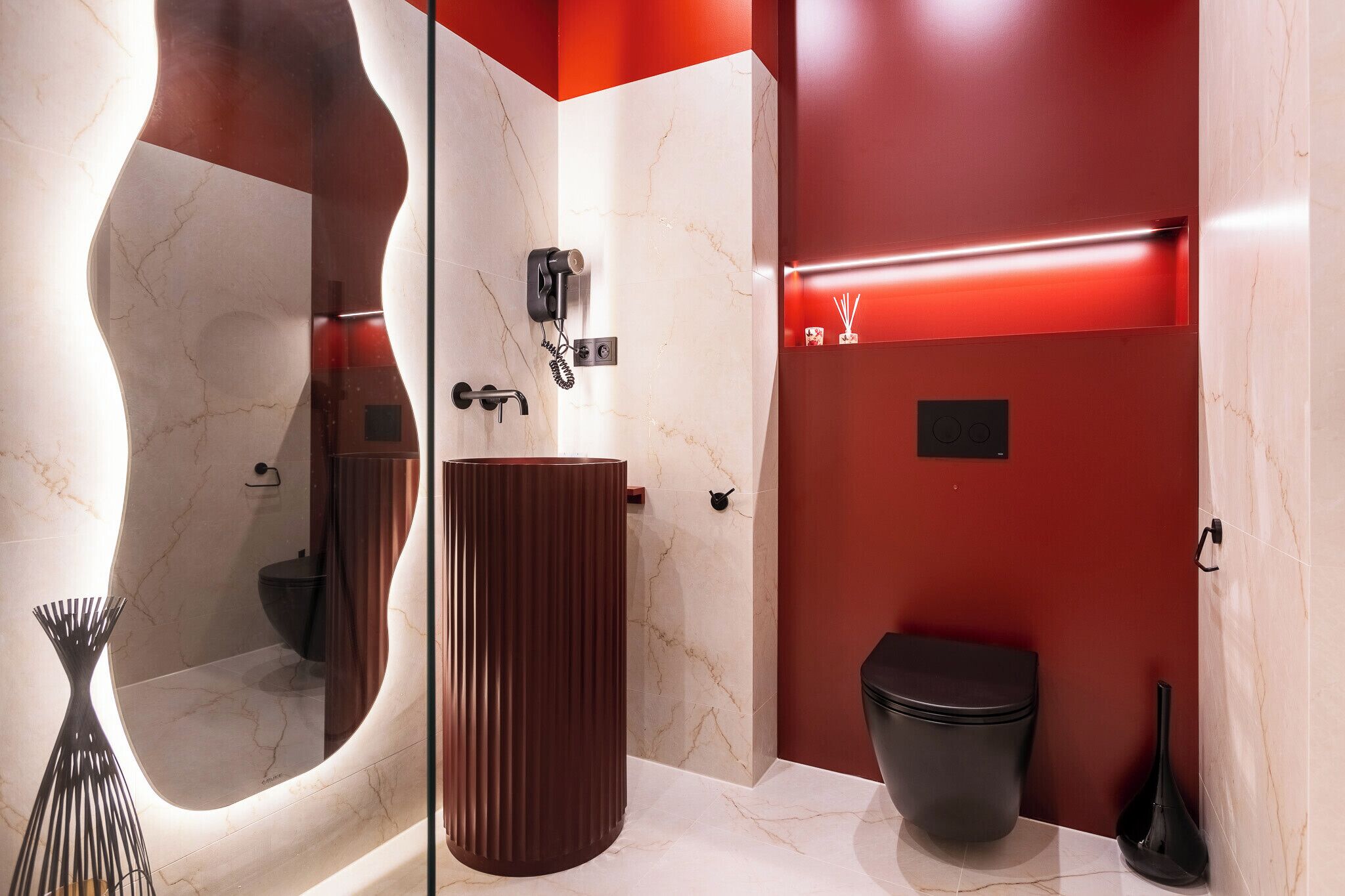 Ein modernes Badezimmer mit Waschtisch aus Marmor, einer schwarzen Toilette und einer roten Akzentwand.