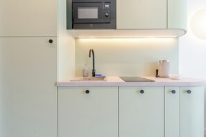 Et moderne køkken med indbygget mikroovn, vask med armatur og en bordplade med en tablet og elkedel.