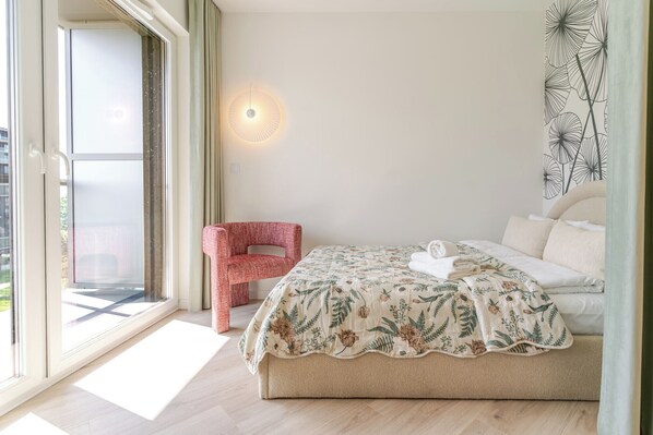 Un dormitorio con cama, una silla, una lámpara de pared y una ventana.