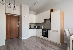 A modern kitchen with white cabinets, a microwave, an oven, and a wooden door.
