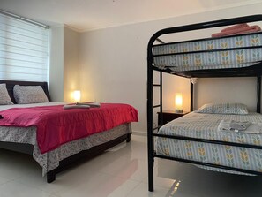 A room with a single bed, a bunk bed, a bedside table with a lamp, and a window with blinds. - PRIVATE KING SUITE / Bunk Beds / Maximum 4 People, Punta Paitilla (Panamá)