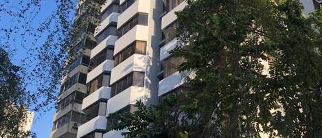 A multi-story building with balconies, surrounded by trees.