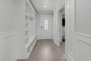 Un pasillo con paredes blancas, suelo de madera y una puerta con un panel de vidrio decorativo.